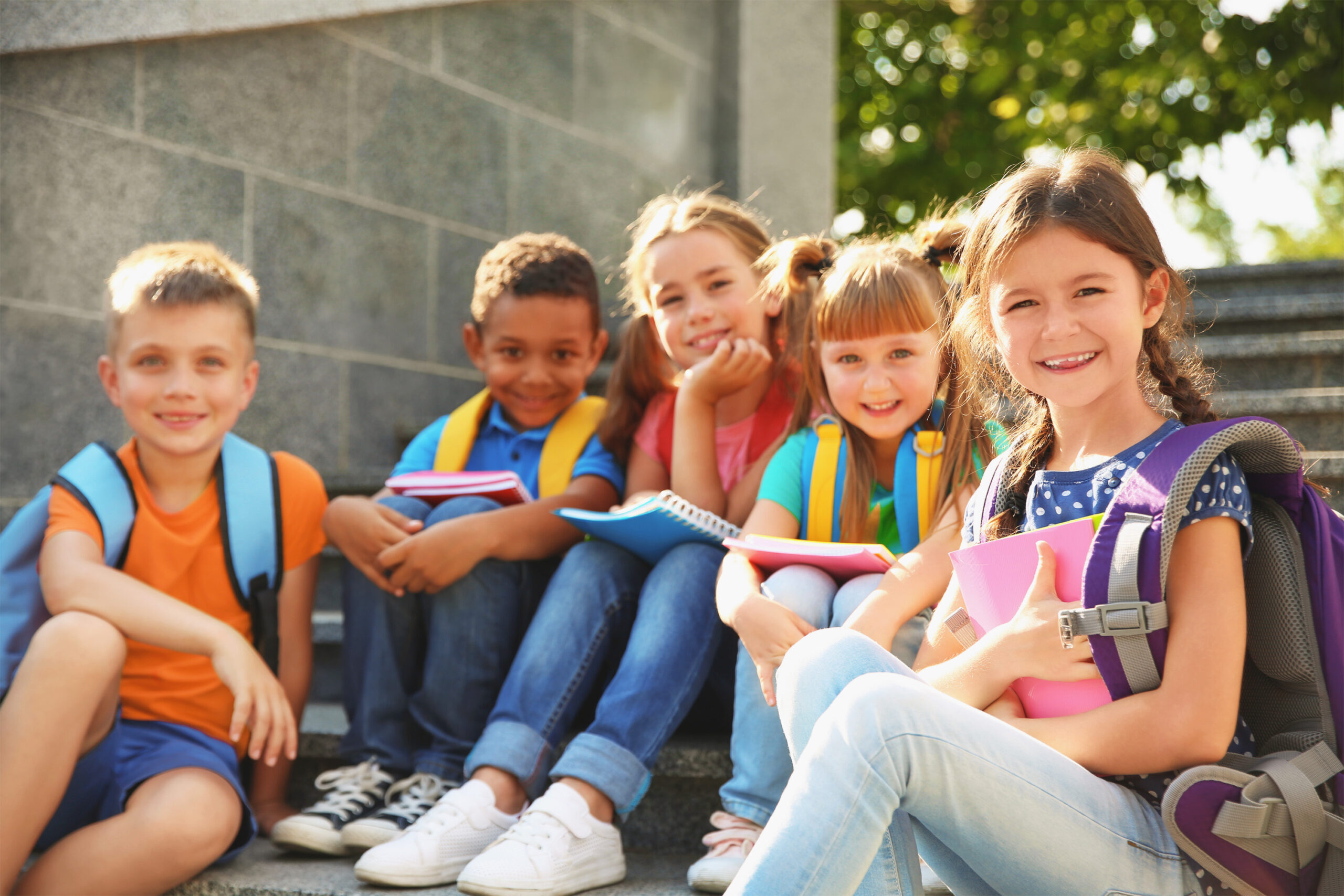 Young students with backpacks and notebooks sitting on steps outside.